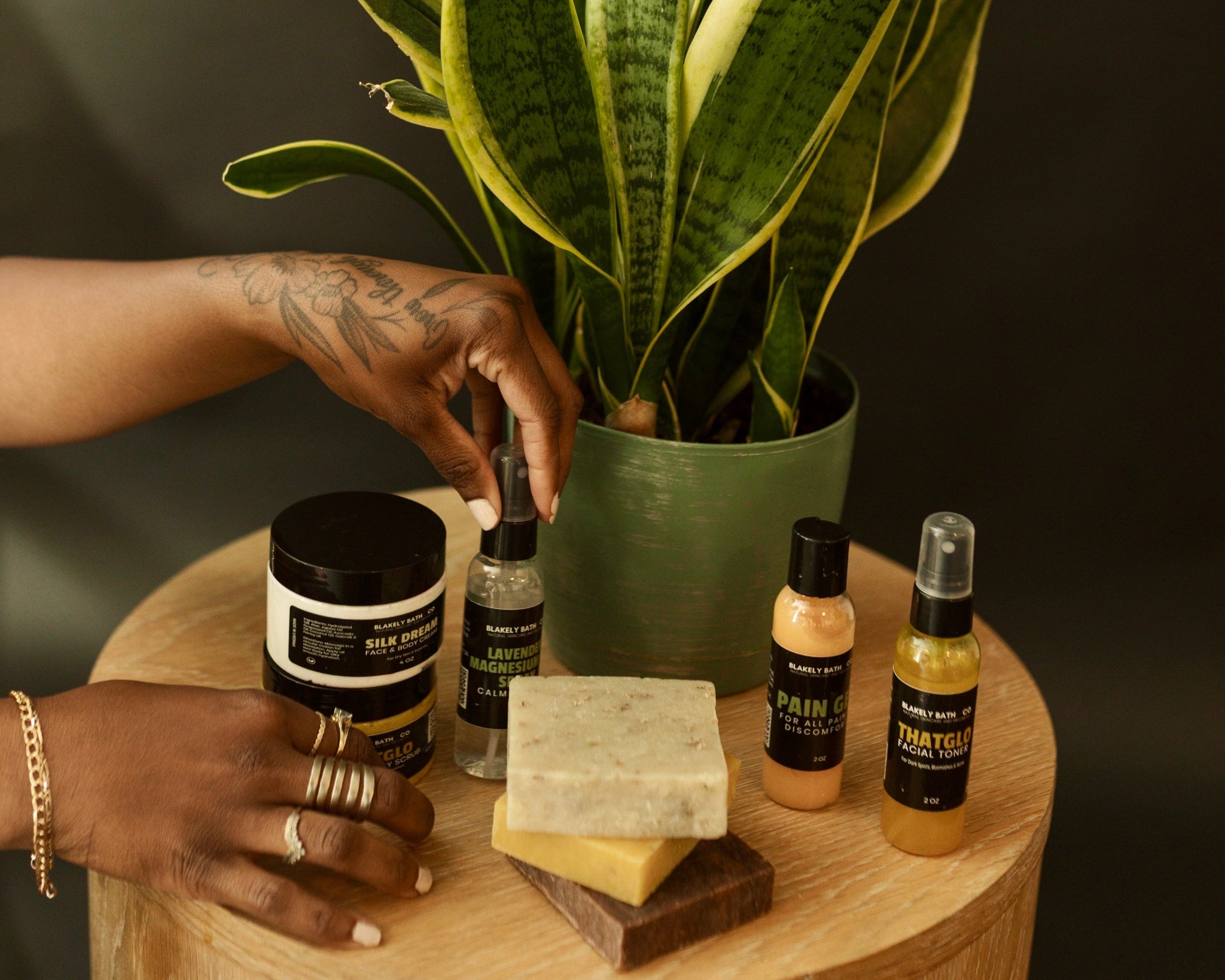 Woman reaching for Lavender Magnesium Spray with plant and skincare products on a wooden table