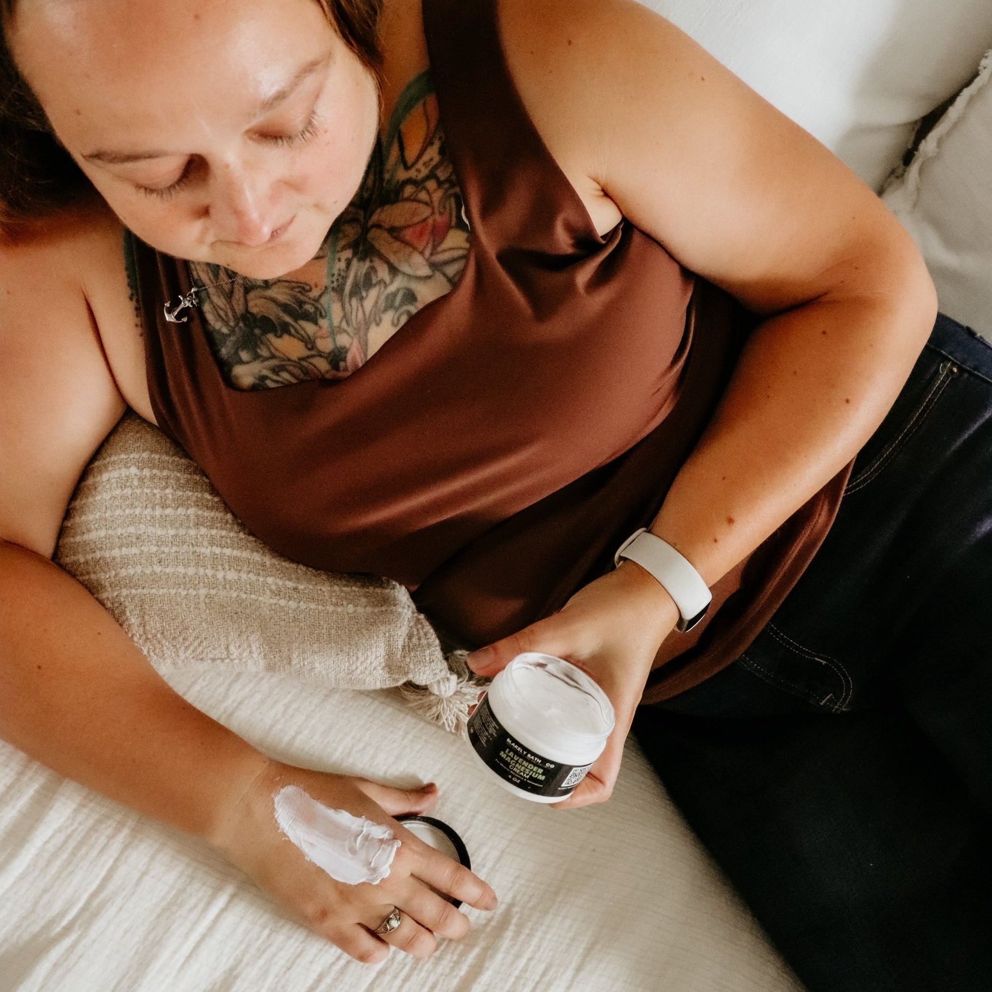 Woman applying cream to her hand on a bed