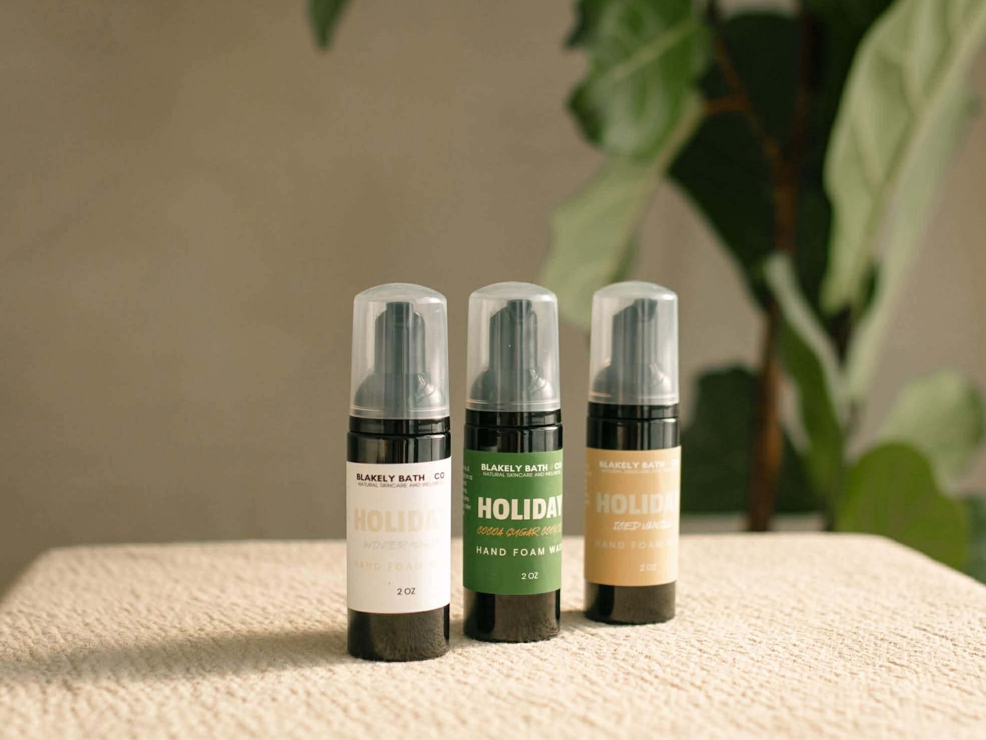 Three bottles of 'Natalie's Bath' products on a textured surface with a plant in the background.