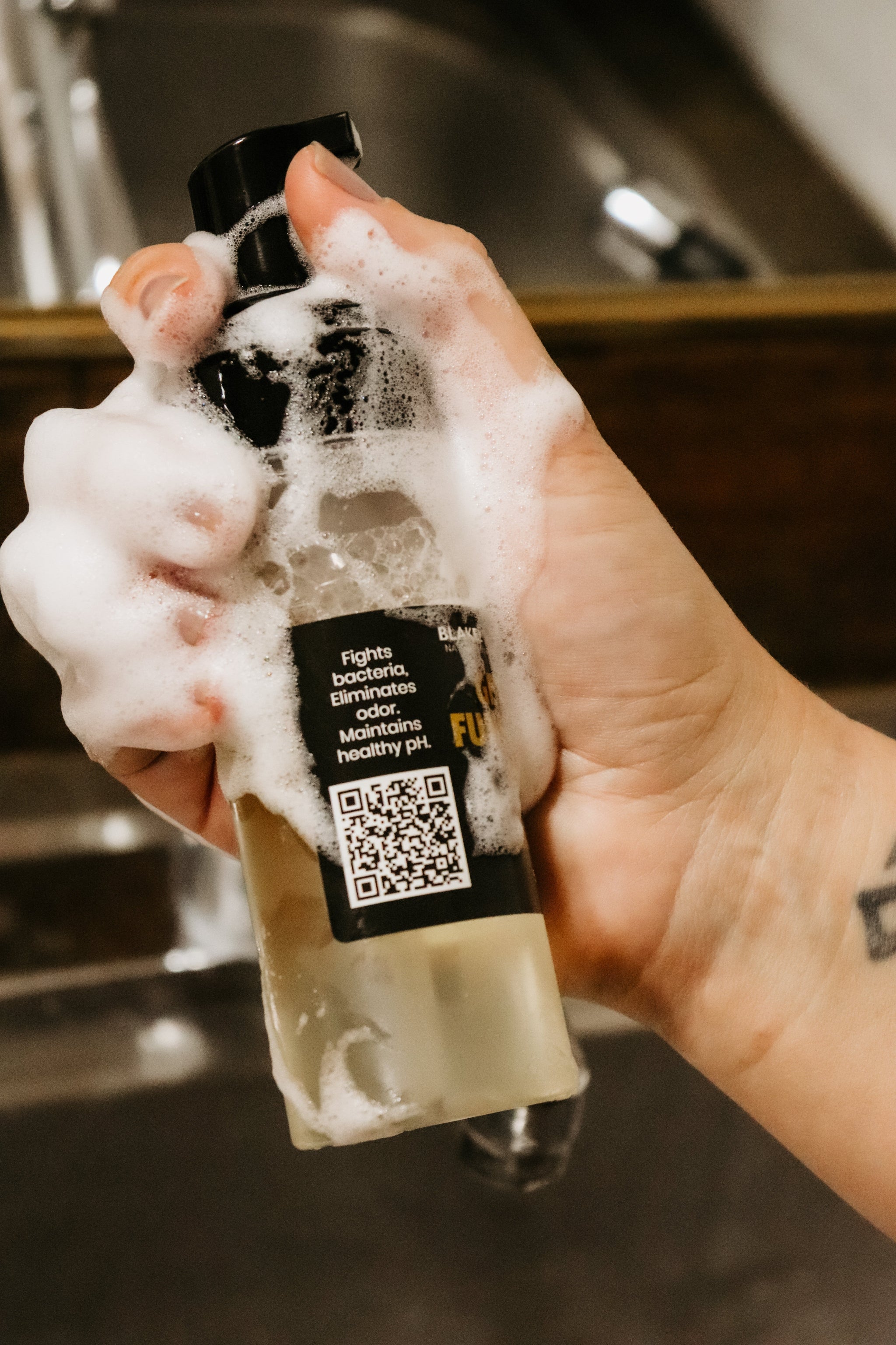 Girl holding Blakely Bath & Co Feminine Foam Wash bottle with soap lathered on her hand and the bottle, demonstrating the rich foam, use and scannable QR code 