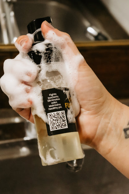 Girl holding Blakely Bath & Co Feminine Foam Wash bottle with soap lathered on her hand and the bottle, demonstrating the rich foam, use and scannable QR code 