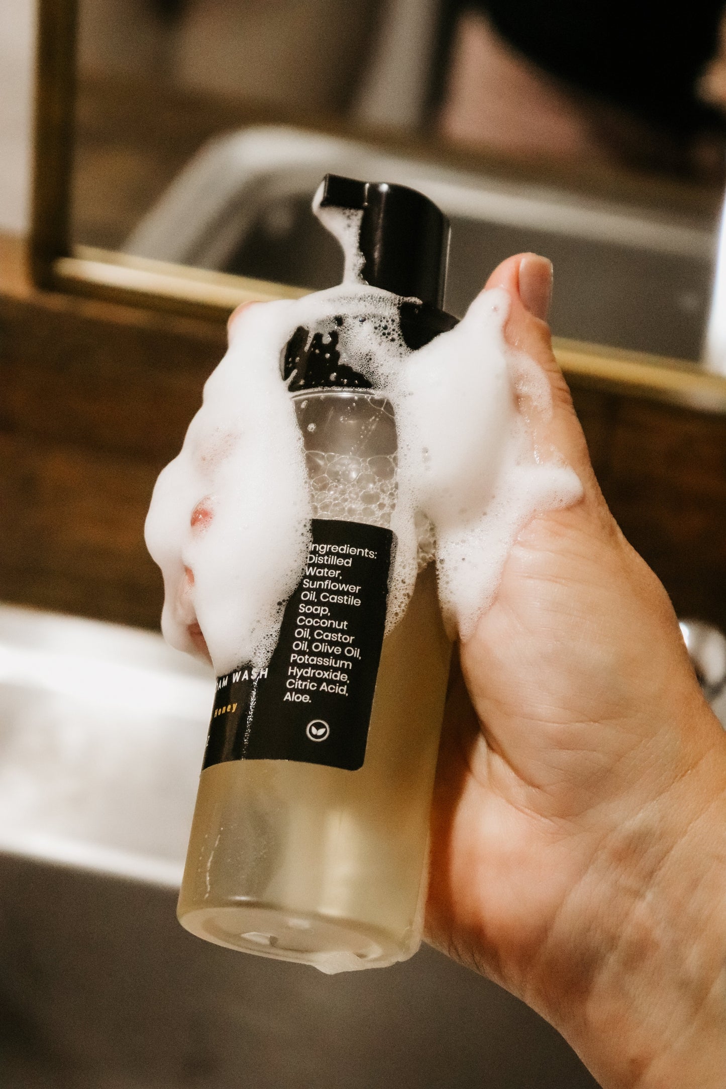 Girl holding Blakely Bath & Co Feminine Foam Wash bottle with soap lathered on her hand and the bottle, demonstrating the rich foam and gentle plant based formula 