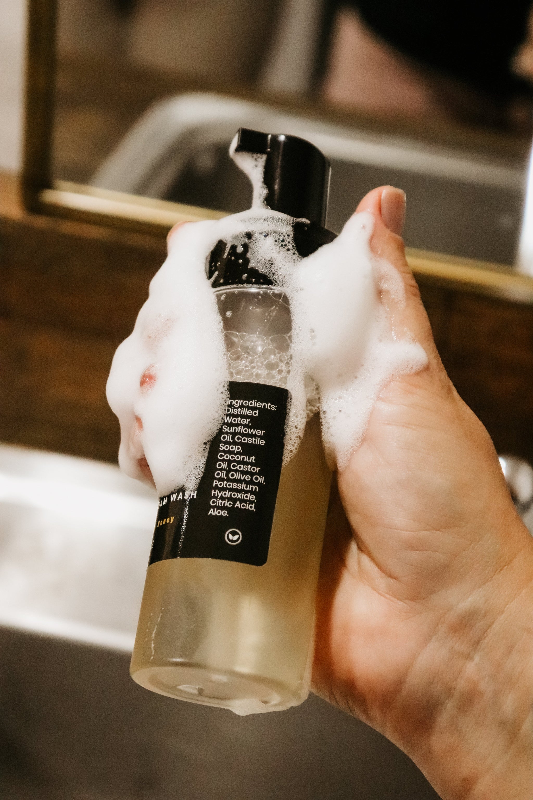 Girl holding Blakely Bath & Co Feminine Foam Wash bottle with soap lathered on her hand and the bottle, demonstrating the rich foam and gentle plant based formula 