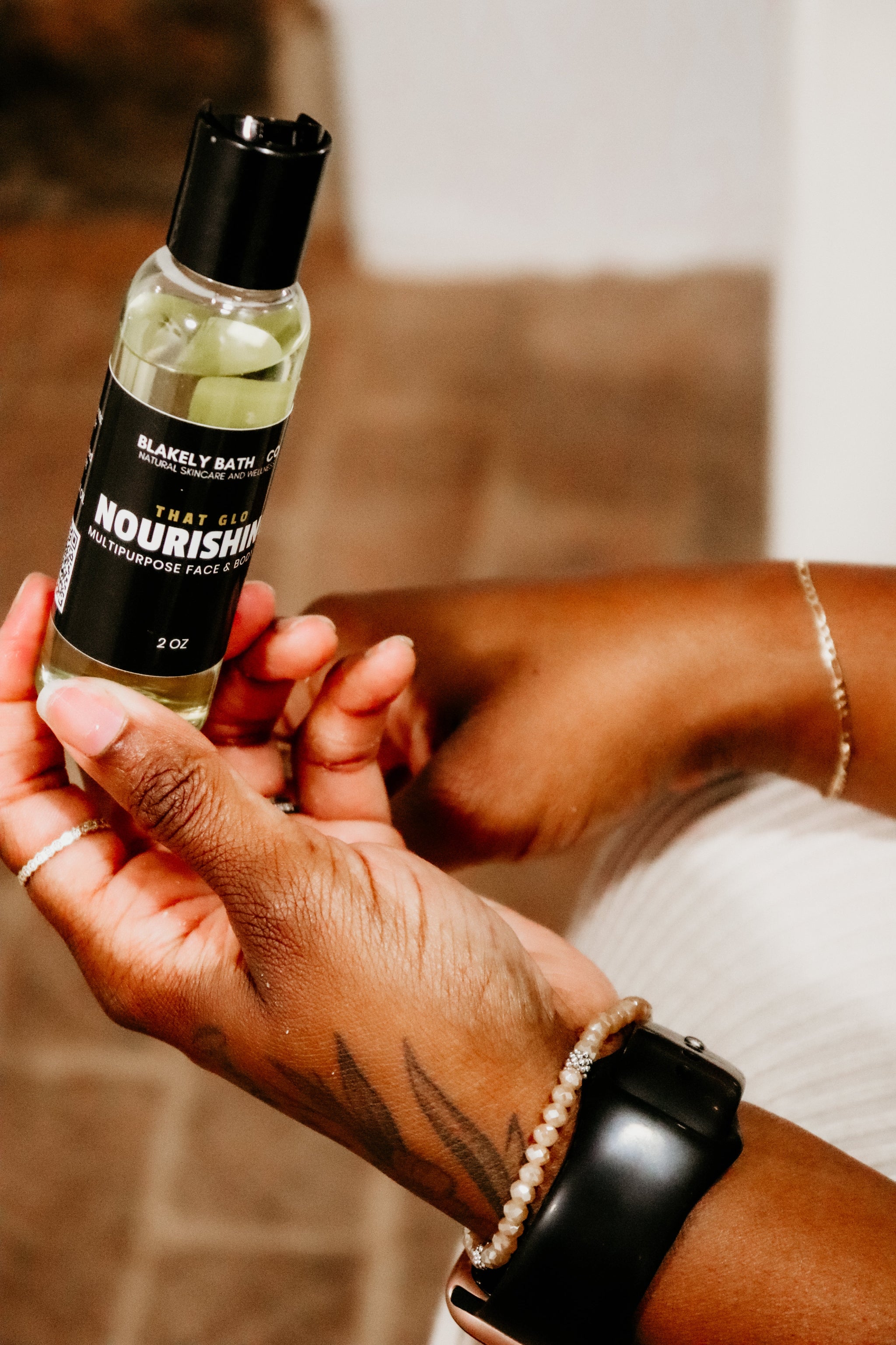 Hand holding a bottle of 'Blakely Bath Co.' nourishing face and body oil with a blurred background