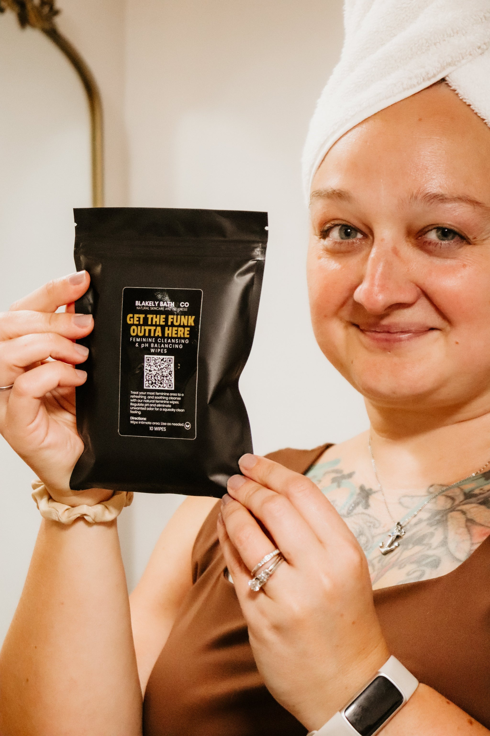 Woman holding Blakely Bath & Co Feminine Cleansing & pH Balancing Wipes, with white wrapped towel on her head