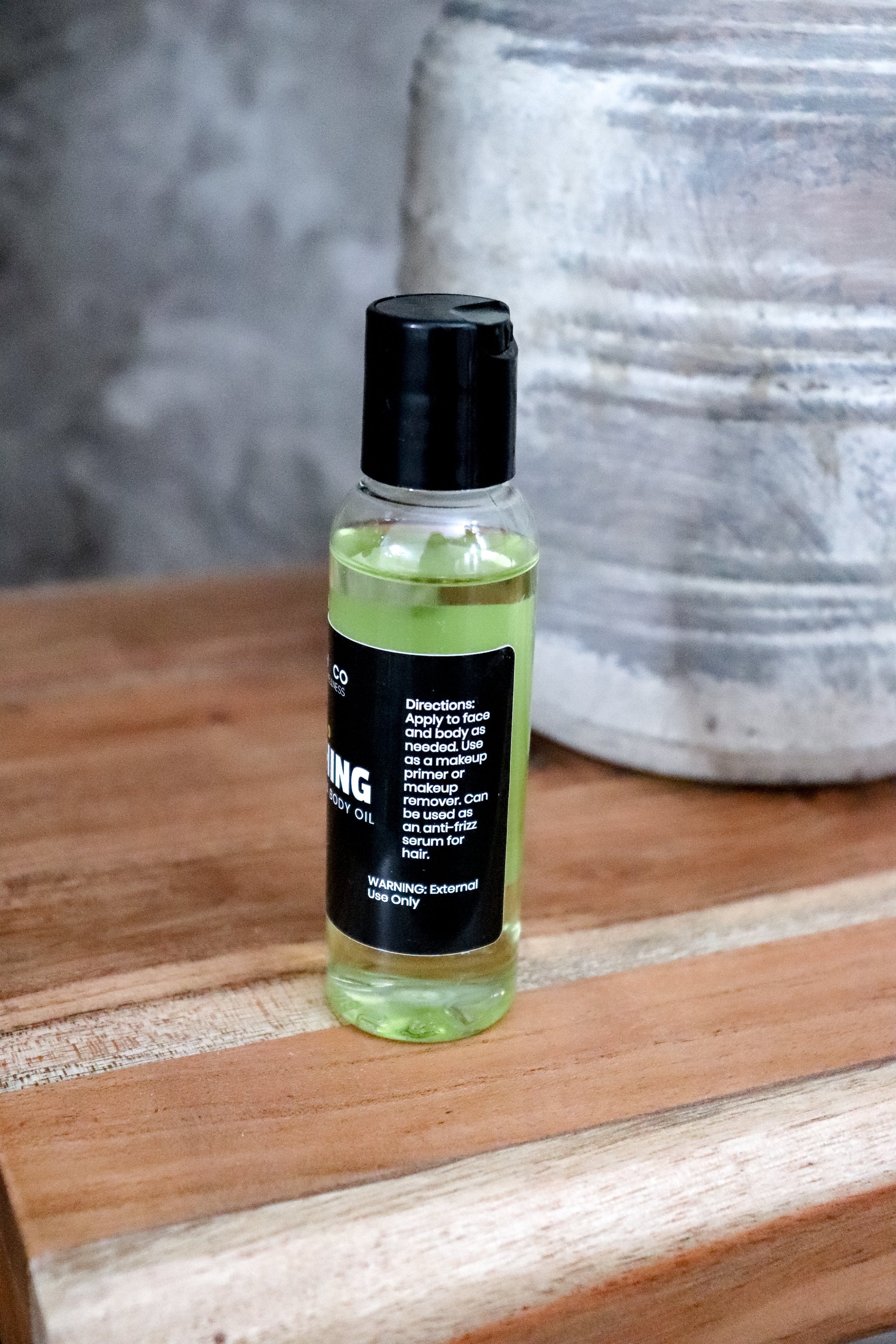 Small bottle of Nourishing face and body oil with black cap showing directions on a wooden surface