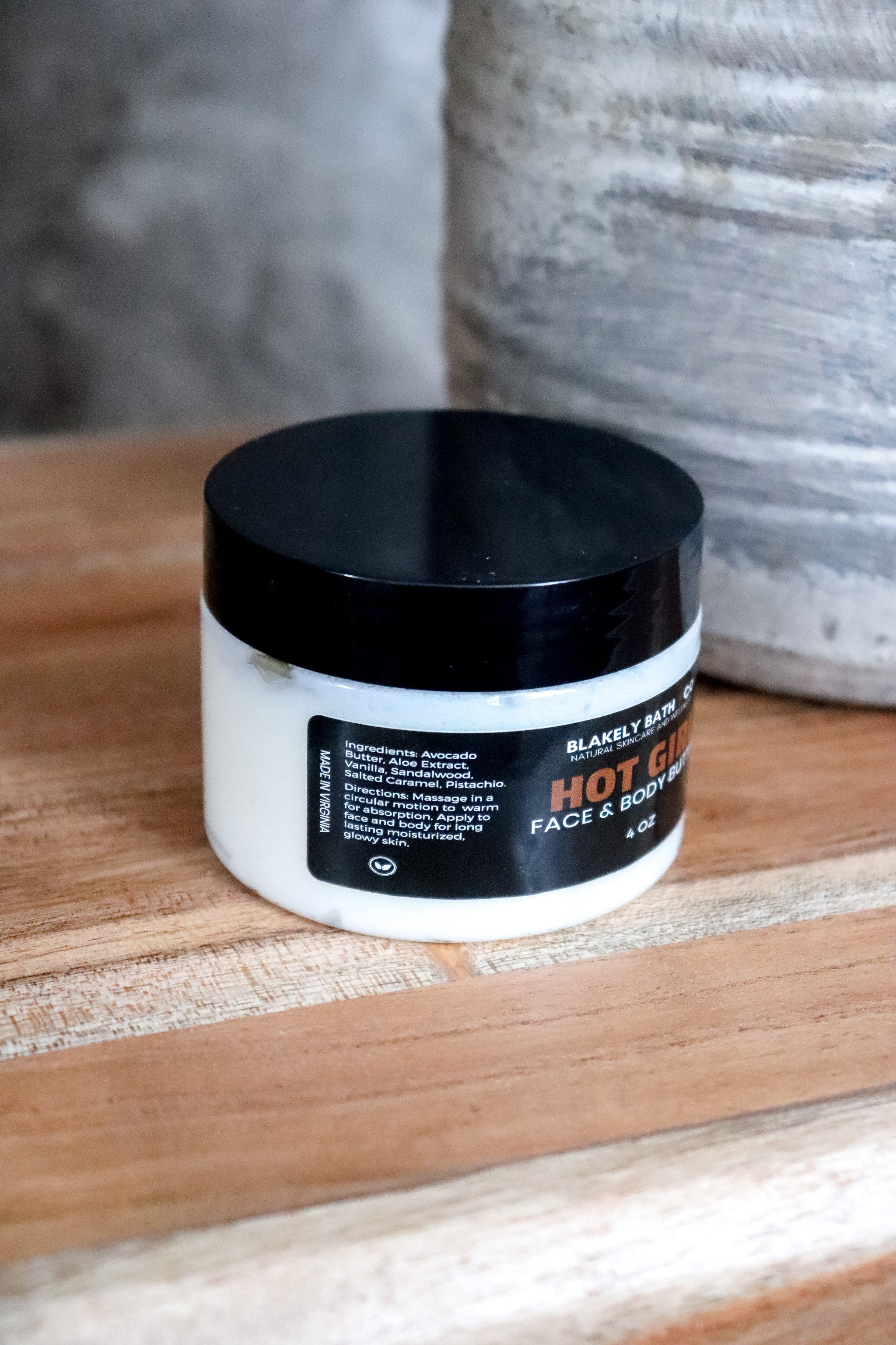 Jar of Hot Girl Face and Body Butter ingredients on label sitting on a wooden surface with a neutral background