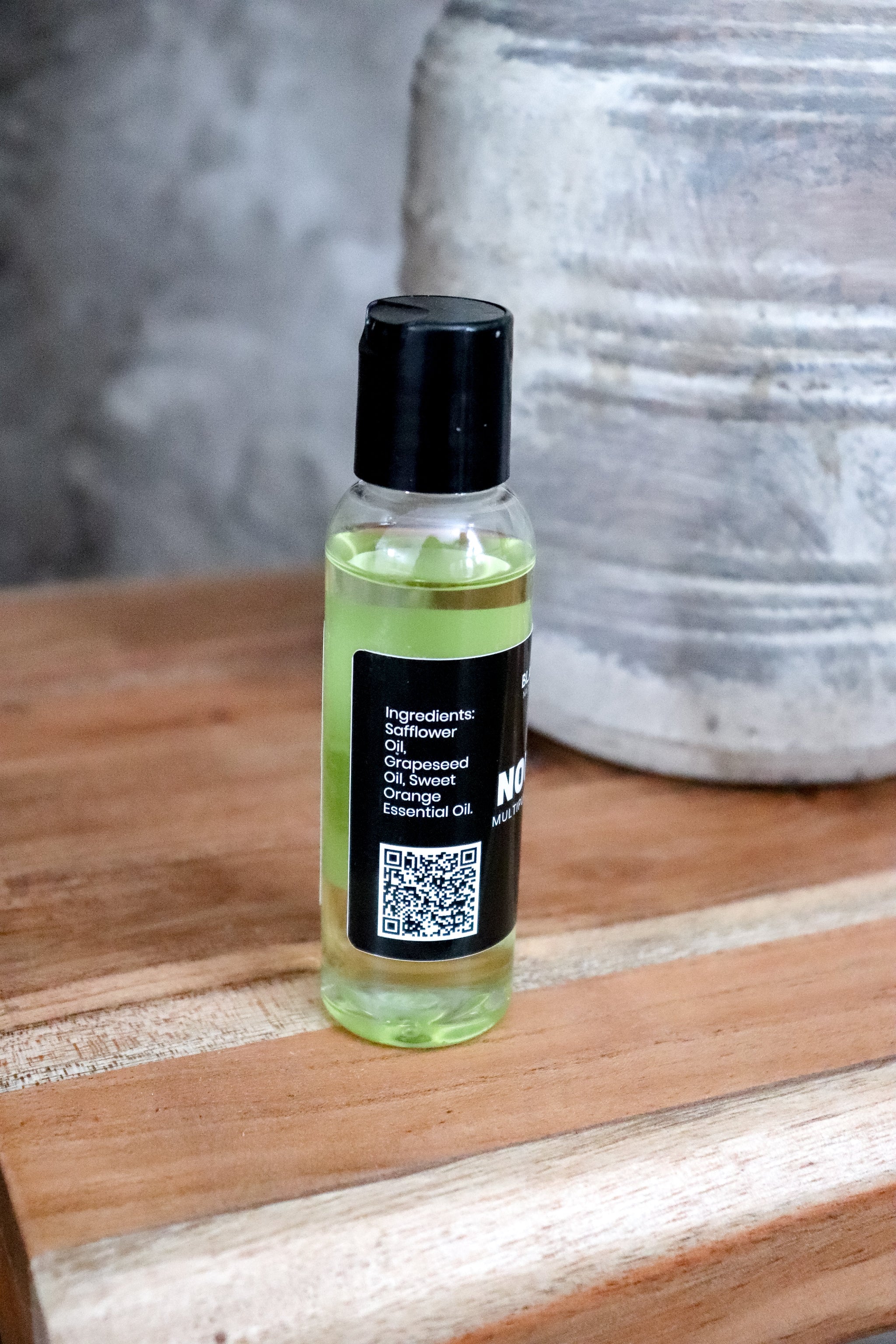 Small bottle of Nourishing Face and Body Oil showing ingredients with a black cap and label on a wooden surface
