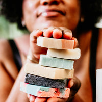 Smiling woman holding a natural bar soap by Blakely Bath & Co, promoting the Soapscription program for Soapscribe members, featuring eco-friendly, skin-nourishing soap bars delivered regularly