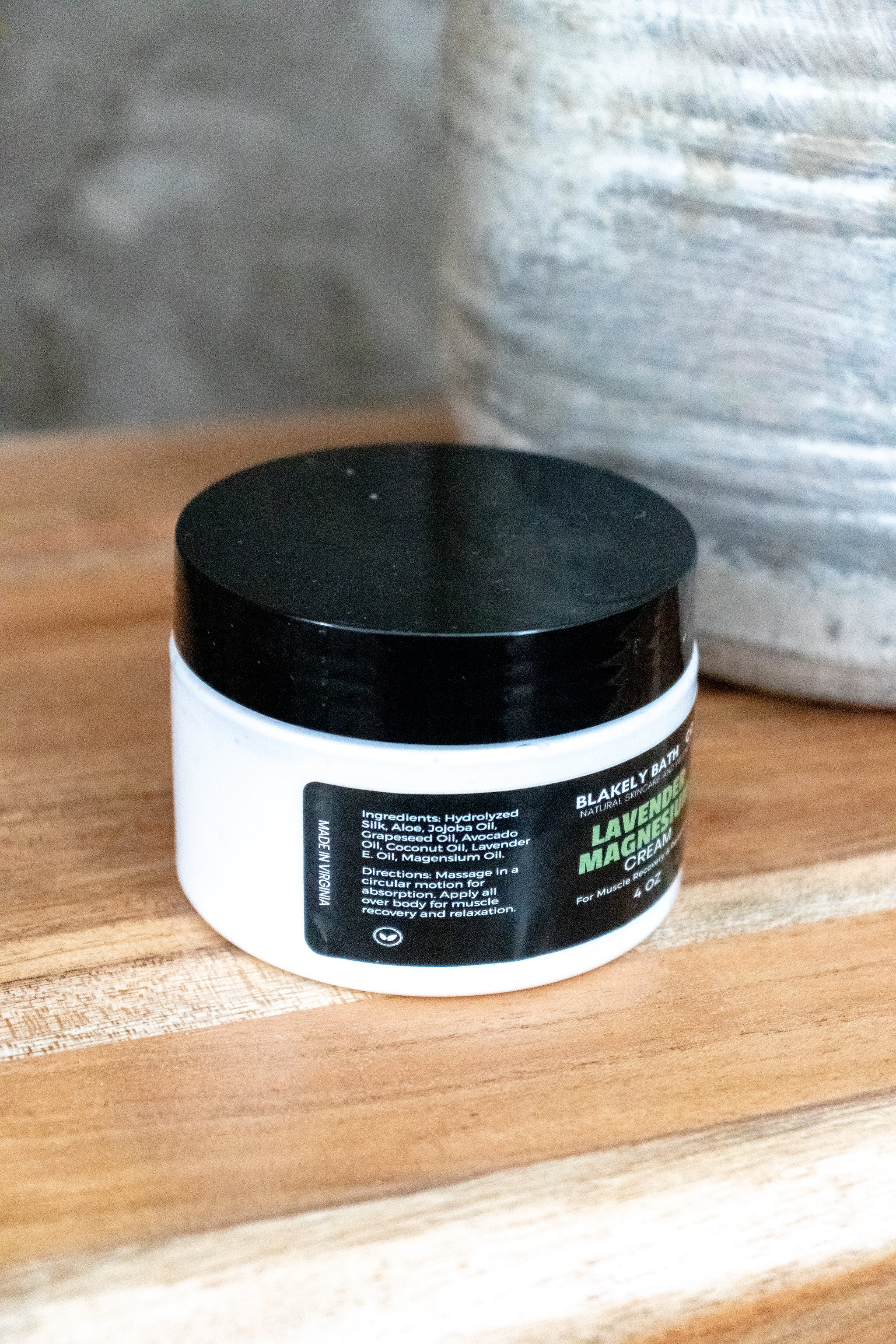 Jar of Lavender Magnesium Cream with black lid on a wooden surface showing directions on use
