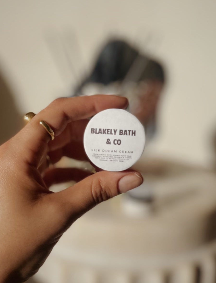 Tessa Chaplin holding a small container of Silk Dream Moisturizing Cream by Blakely Bath & Co, ready to experience the rich, nourishing hydration for soft, smooth skin