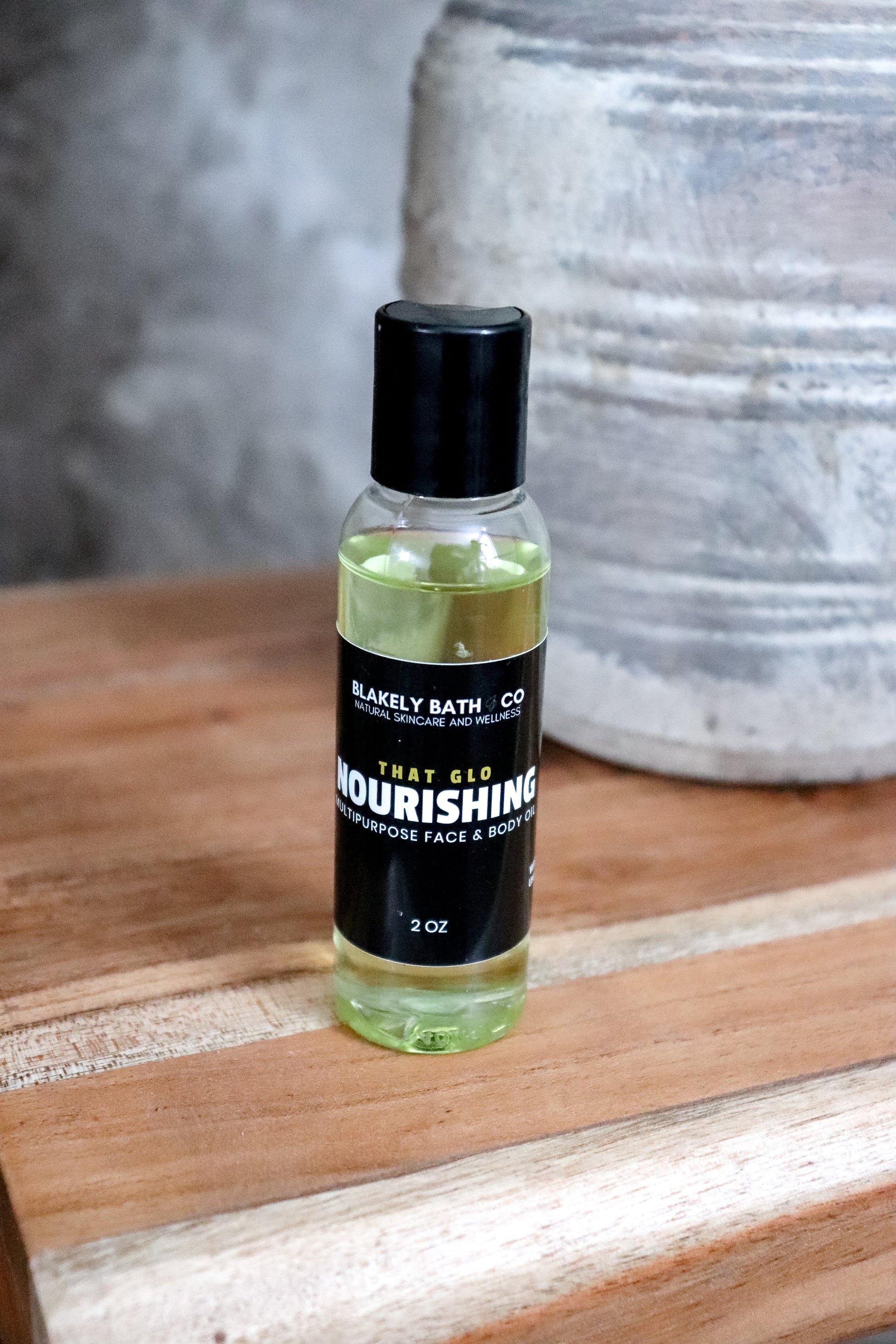 Bottle of Nourishing Face and body oil  on a wooden surface with a blurred background by Blakely Bath & Co 