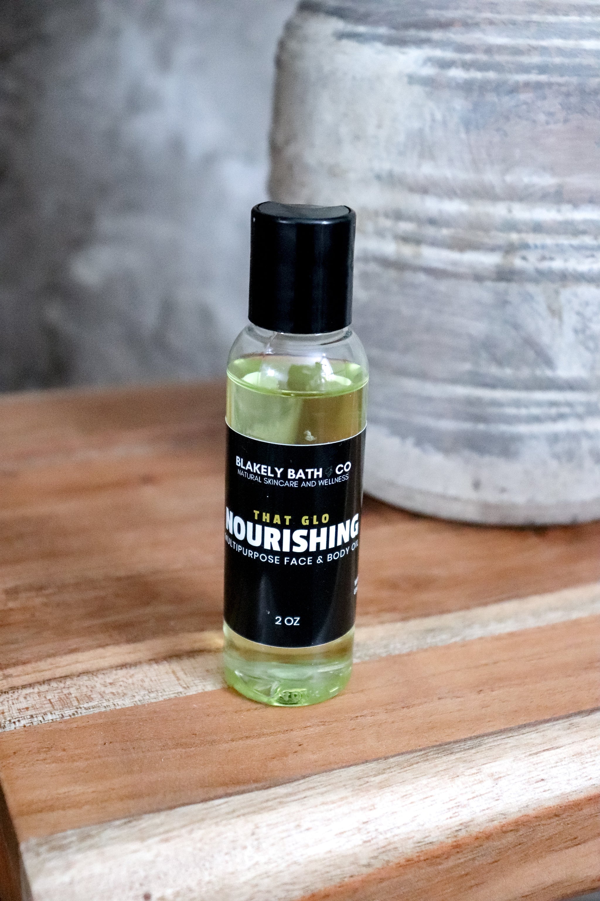 Bottle of Nourishing Face and body oil  on a wooden surface with a blurred background by Blakely Bath & Co 