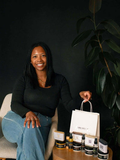 Woman sitting on a chair with a table full of skincare products against a dark background
