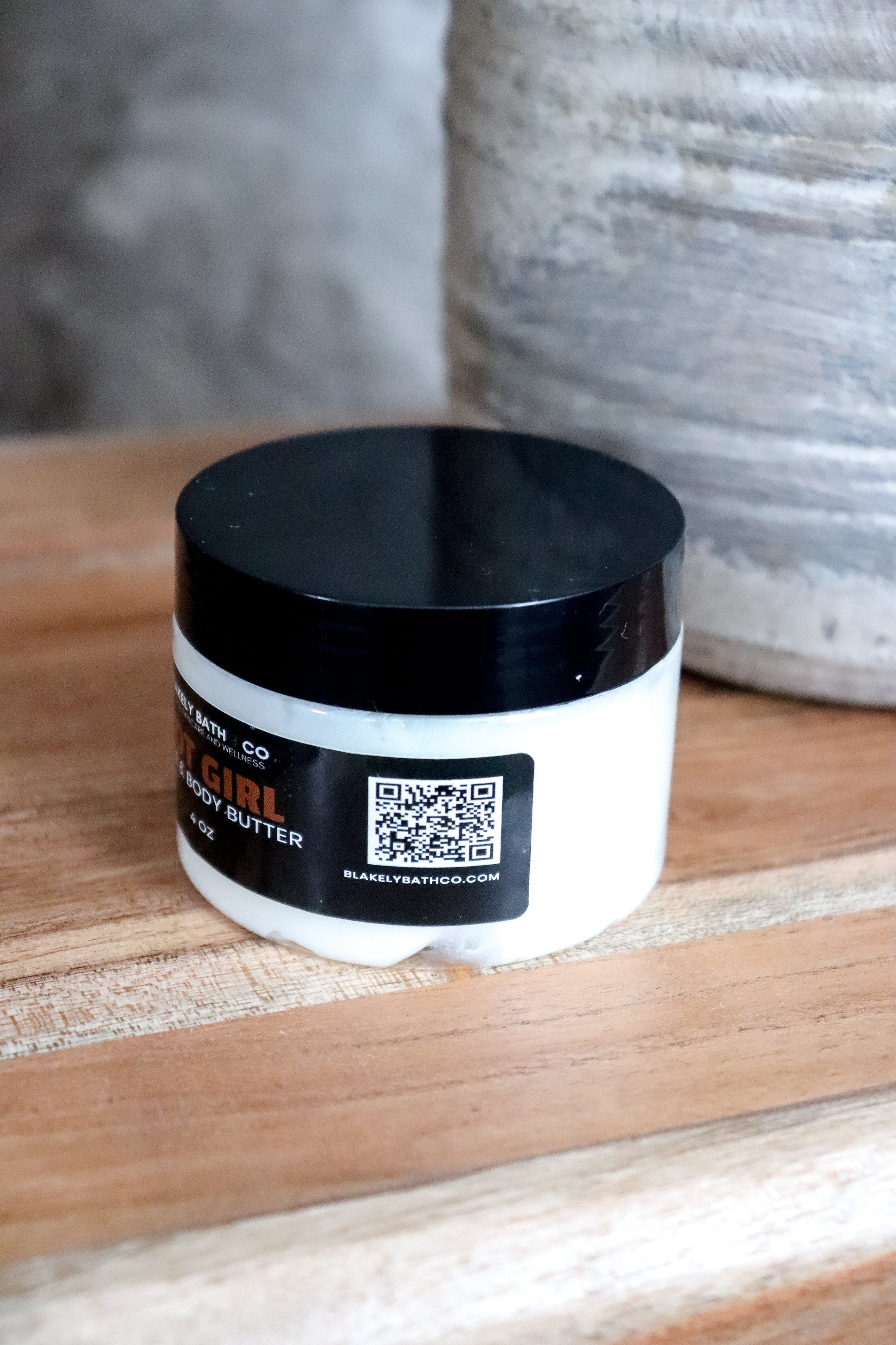 Jar of Hot Girl body butter with a black lid on a wooden surface