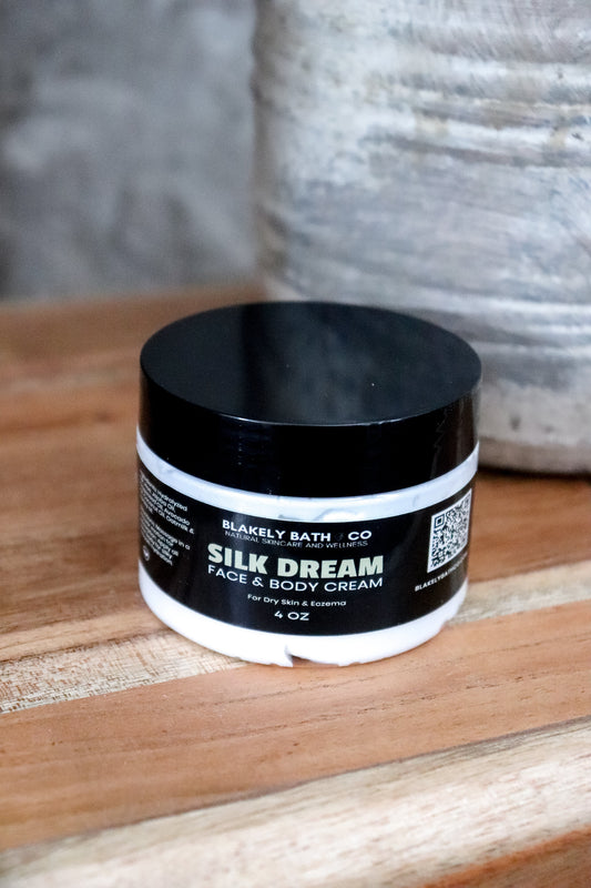 Jar of Blakely Bath Co Silk Dream Face & Body Cream on a wooden surface with a textured gray background best natural skincare moisturizer for radiant, hydrated, and silky smooth skin.