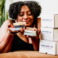 Smiling woman holding a natural bar soap by Blakely Bath & Co, promoting the Soapscription program for Soapscribe members, featuring eco-friendly, skin-nourishing soap bars delivered regularly