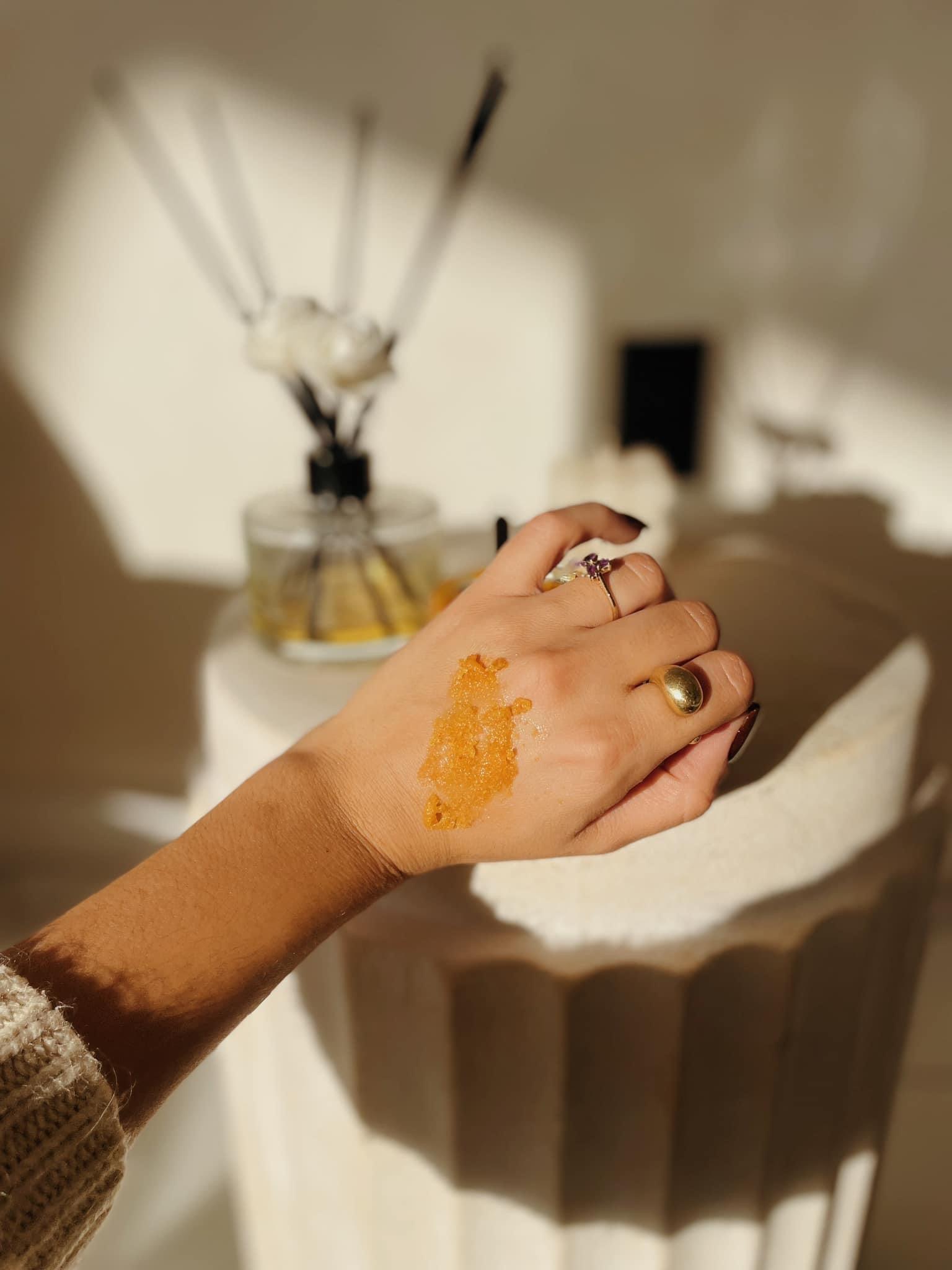 Tessa Chaplin holding a generous amount of ThatGlo Turmeric and Kojic Acid Face and Body Scrub in her hands, showcasing the scrub's creamy texture and golden color, ready to exfoliate for smooth, radiant skin & Co