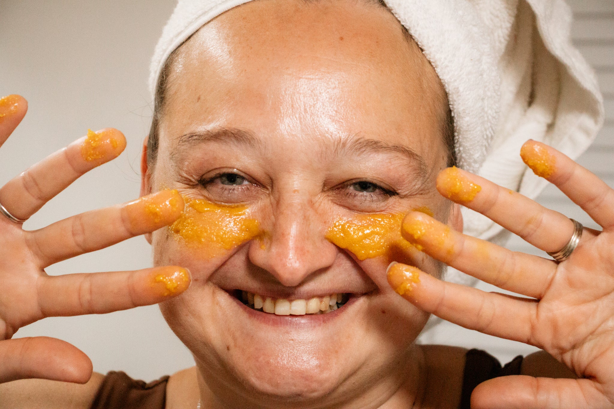 Woman smiling with turmeric brightening scrub from Blakely Bath & Co  on face and fingers