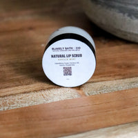Round container of Blakely Bath Co natural vanilla mint liip scrub on a wooden surface