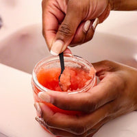 Woman scooping Blakely Bath & Co Cherry Almond Body Scrub while in the bathtub, enjoying the exfoliating and hydrating benefits of the scrub for smooth, soft skin with a sweet cherry almond scent