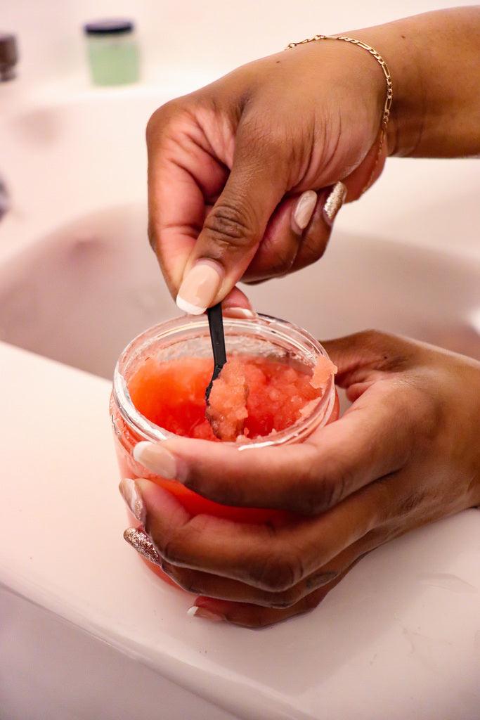 Woman scooping Blakely Bath & Co Cherry Almond Body Scrub while in the bathtub, enjoying the exfoliating and hydrating benefits of the scrub for smooth, soft skin with a sweet cherry almond scent